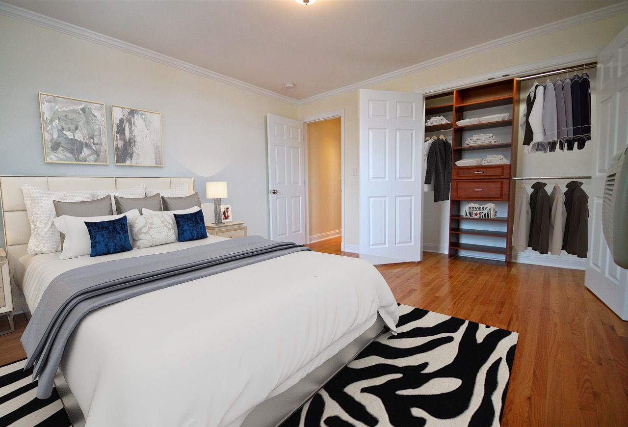 Bright bedroom with a large bed and an open closet displaying clothes.
