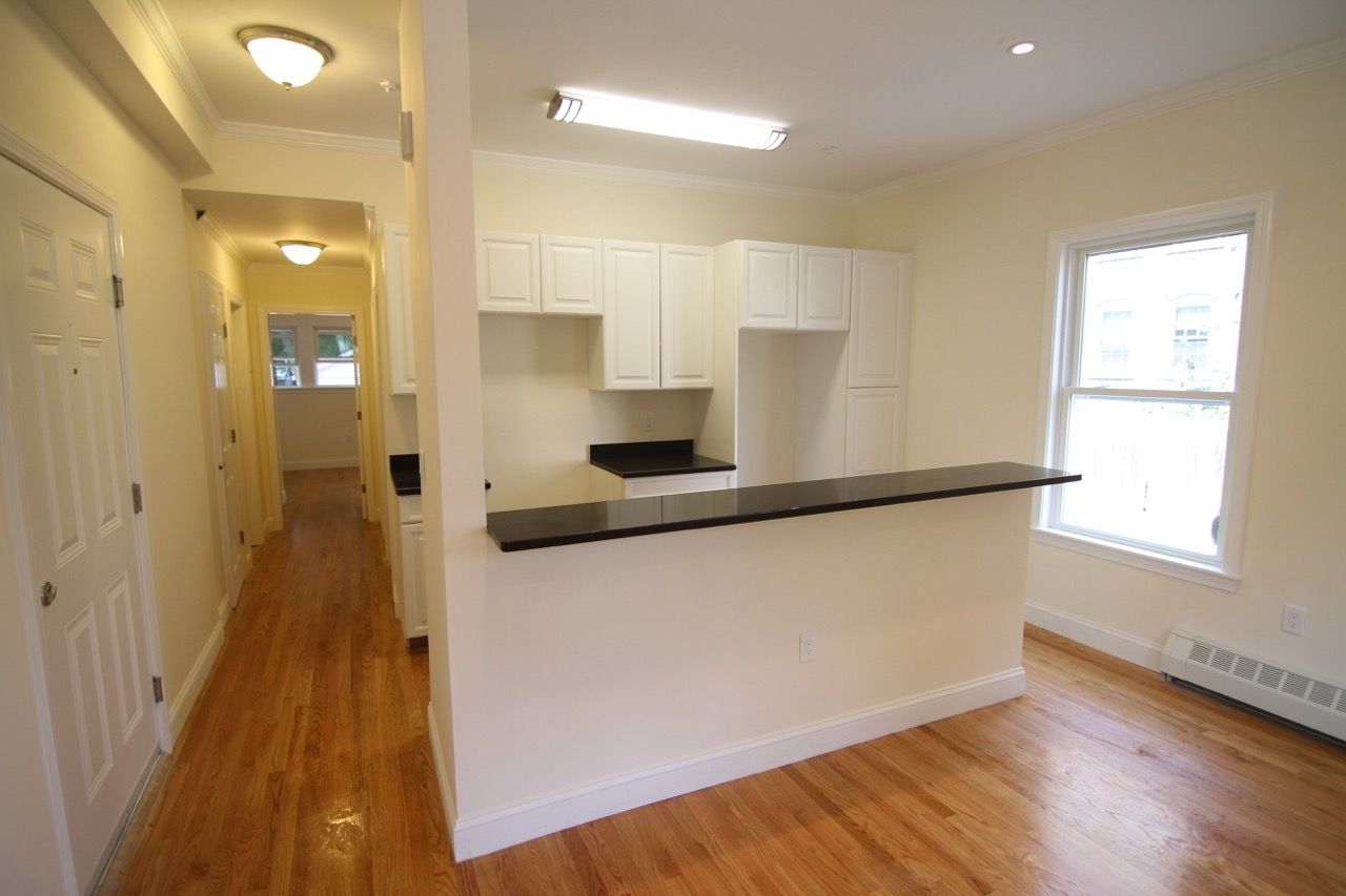 Bright kitchen with white cabinets, a black countertop bar, and hardwood floors in an open-plan apartment.