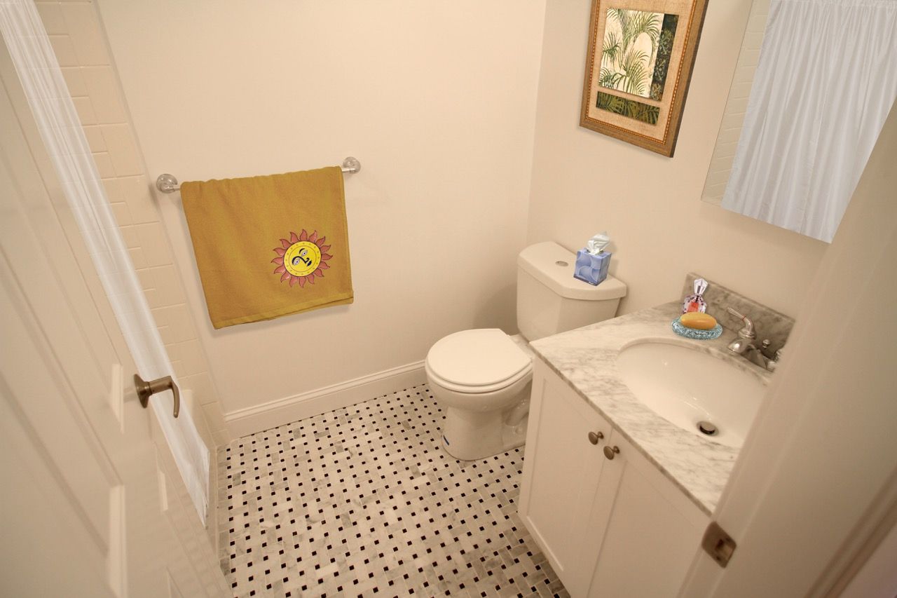 Compact apartment bathroom with toilet, marble vanity, and a yellow sun-themed towel.