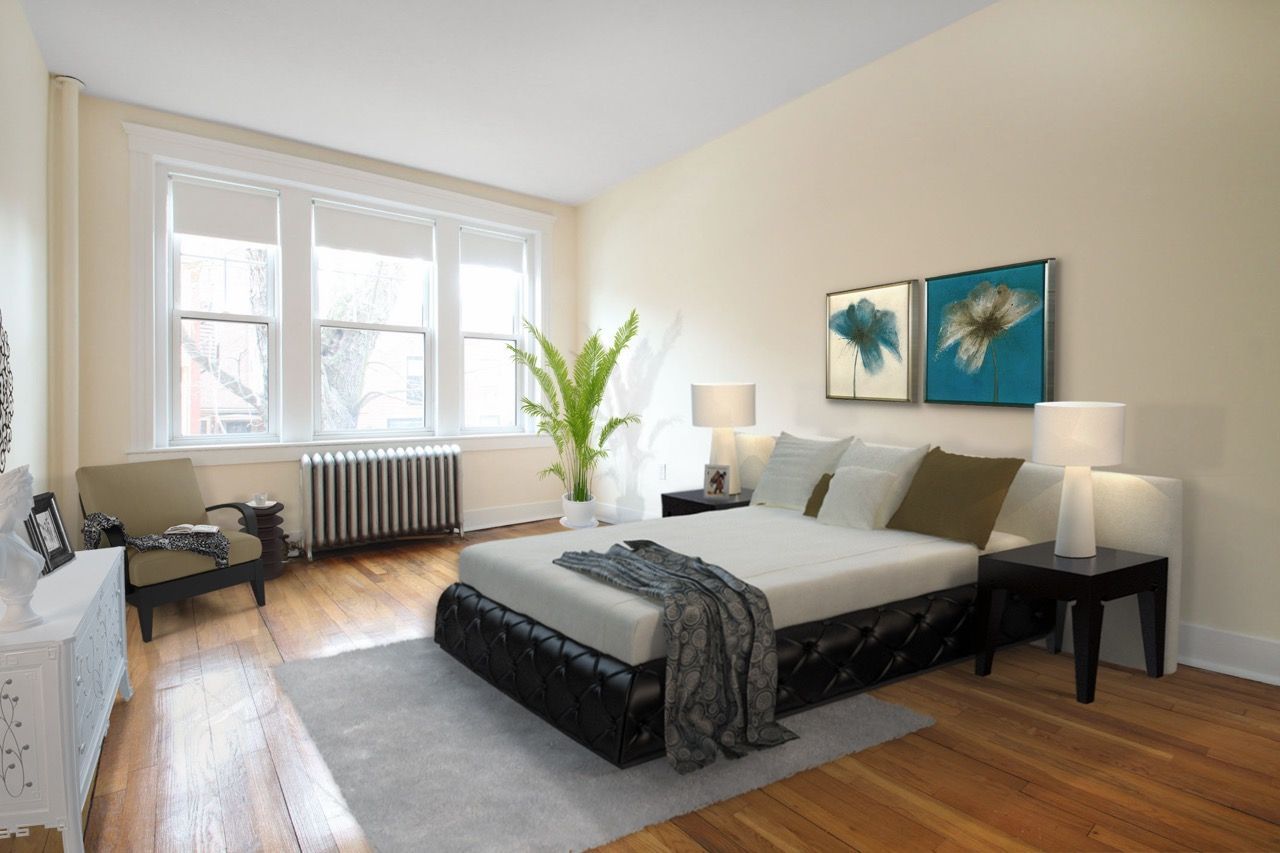Bedroom inside an apartment with a low tufted bed, nightstands, large windows, and hardwood floors.