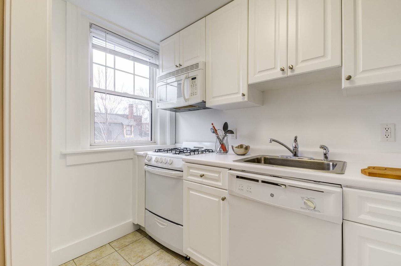 White kitchen with gas stove, microwave, dishwasher, and sink under a window.