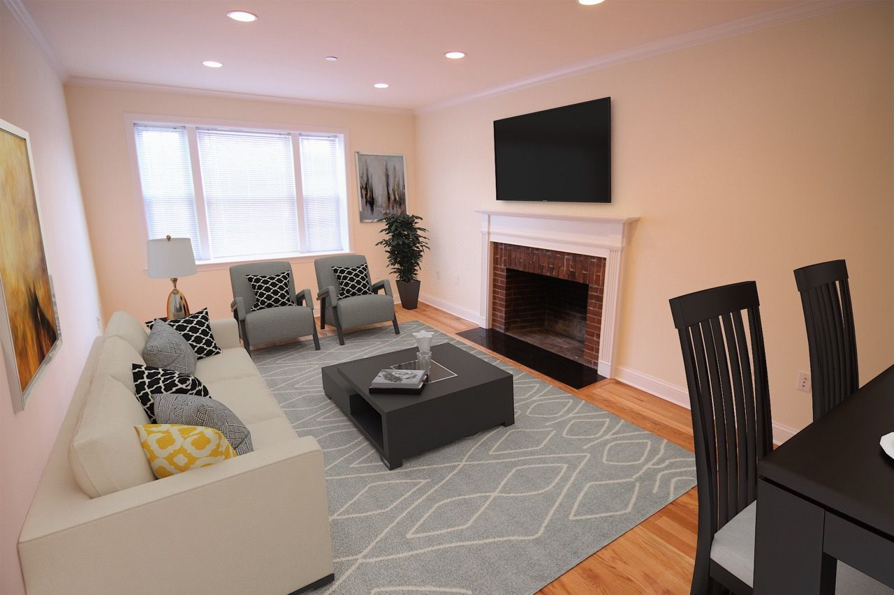 Living room in an apartment with white sofa, two chairs, coffee table, fireplace, and mounted TV.