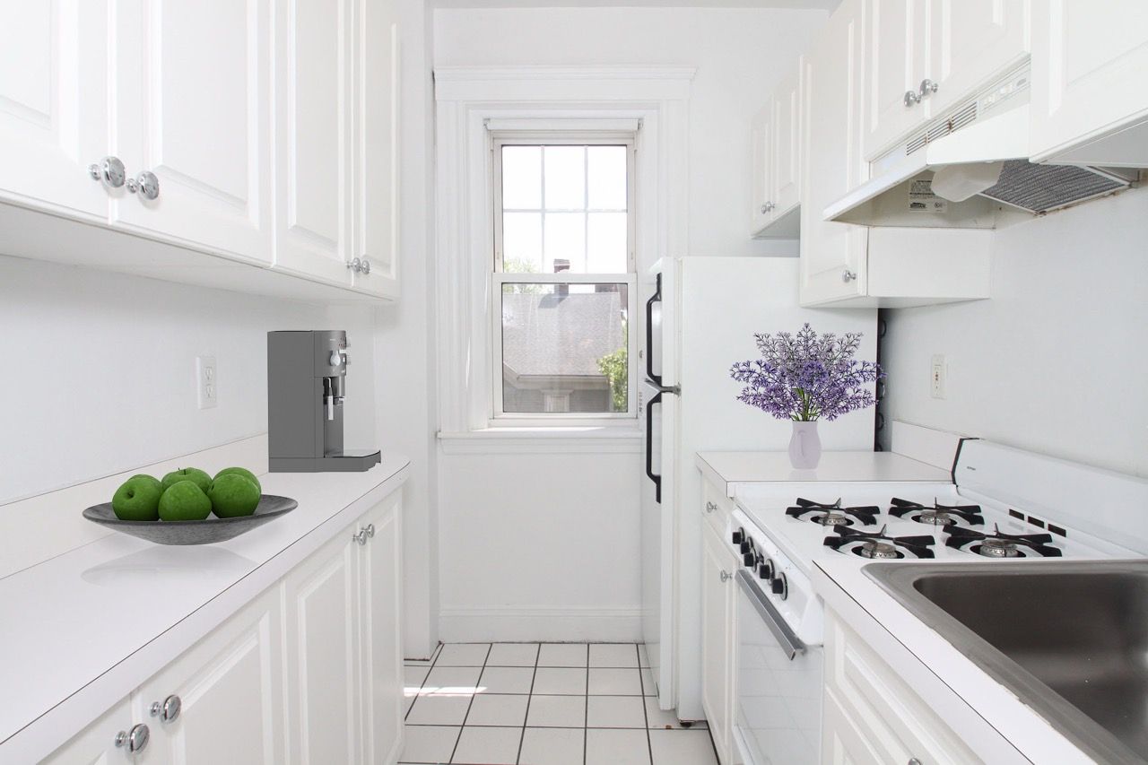 White galley kitchen with cabinets, stove, sink, and a window.