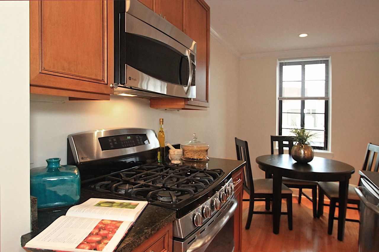 Kitchen with stainless-steel stove and microwave, wooden cabinets, and a round dining table by a window.