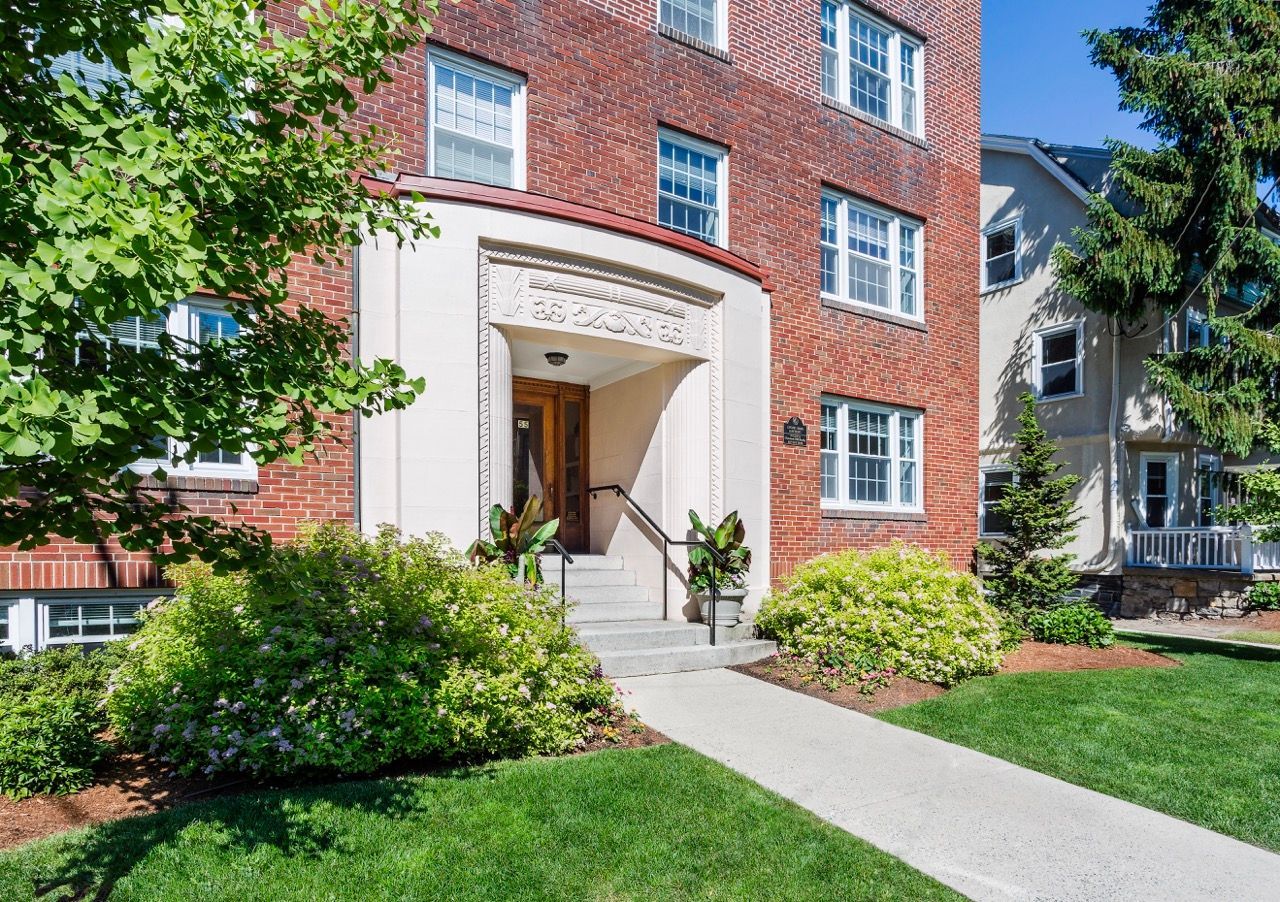 Entrance to a brick apartment building with a decorative stone surround and landscaped front yard.