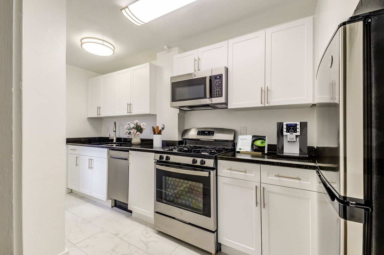 Modern white kitchen with stainless steel appliances and black granite countertops.