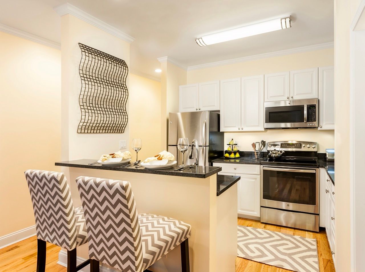 Modern white kitchen with stainless steel appliances, a breakfast bar, and two chevron-patterned chairs.