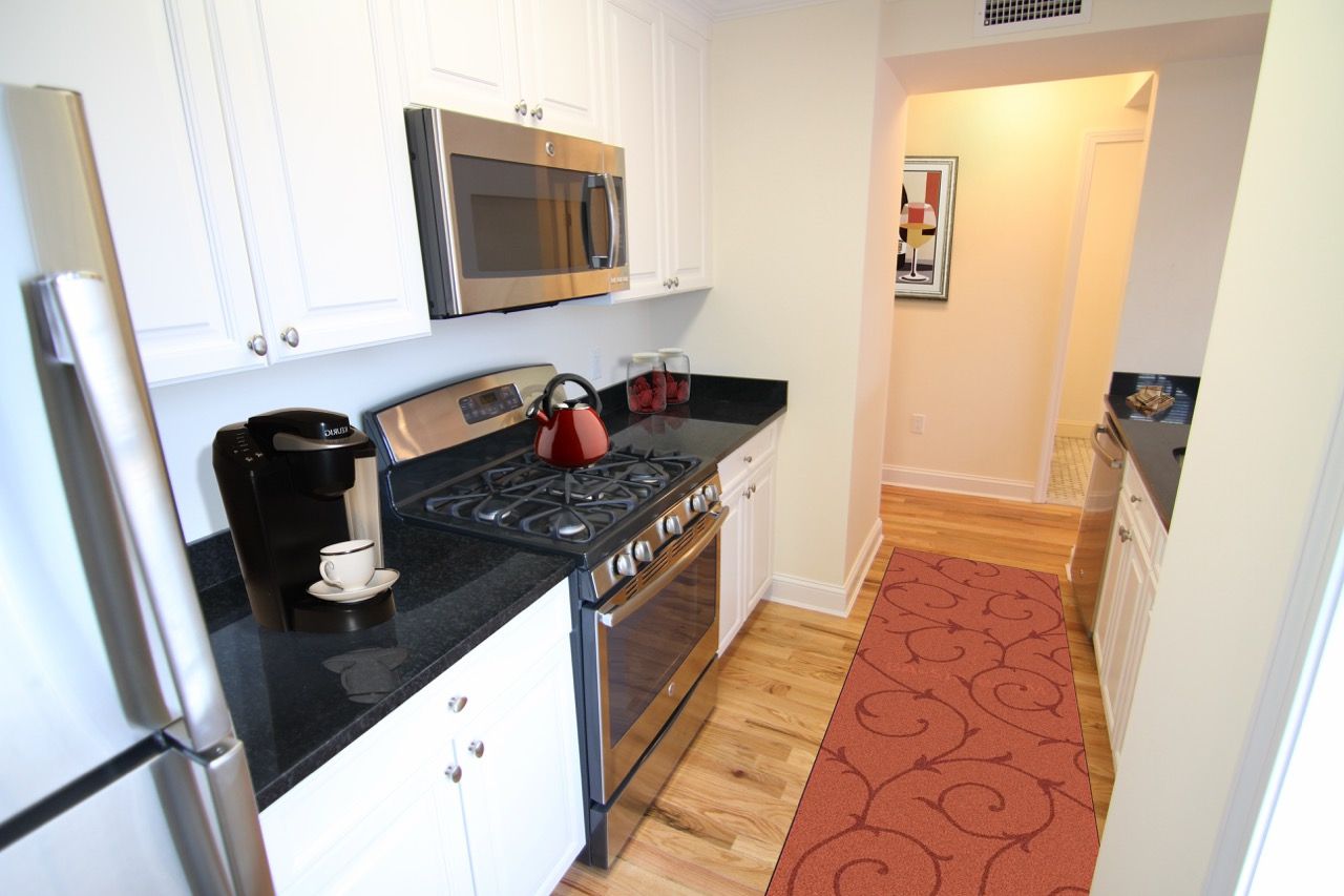 Modern apartment kitchen with white cabinets, stainless appliances, black countertops, and a red kettle.
