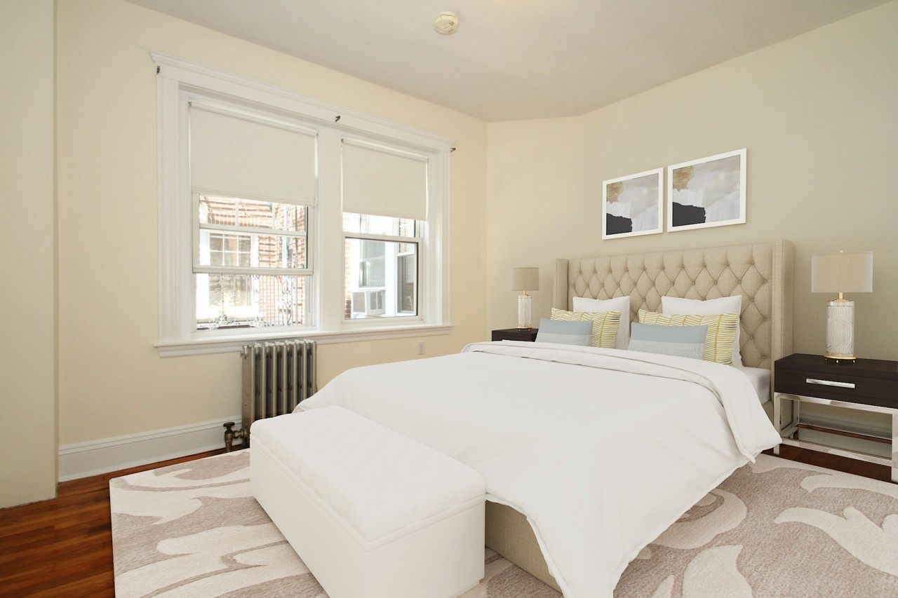 Bedroom in a modern apartment with a tufted headboard, nightstands, and large windows.