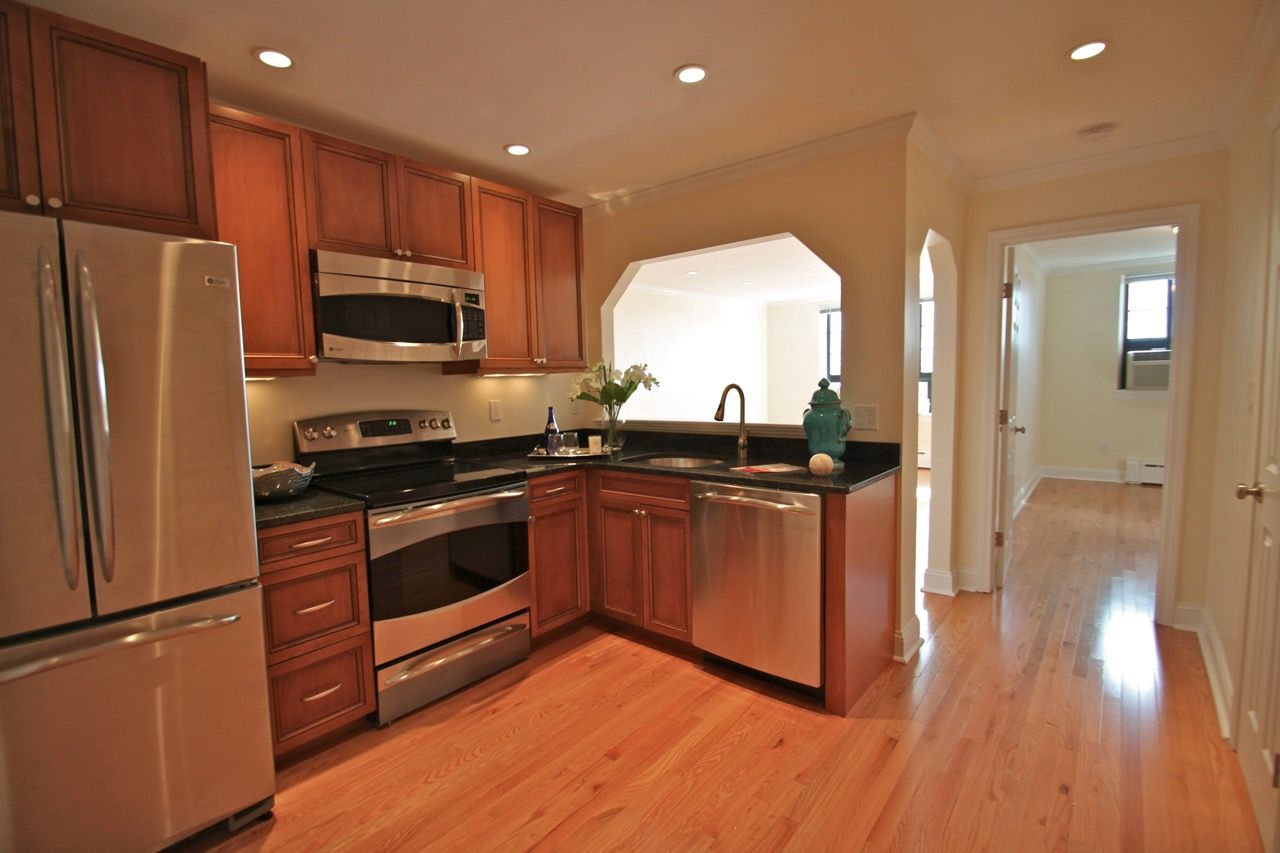 Modern apartment kitchen with stainless steel appliances, wood cabinetry, and dark countertops.