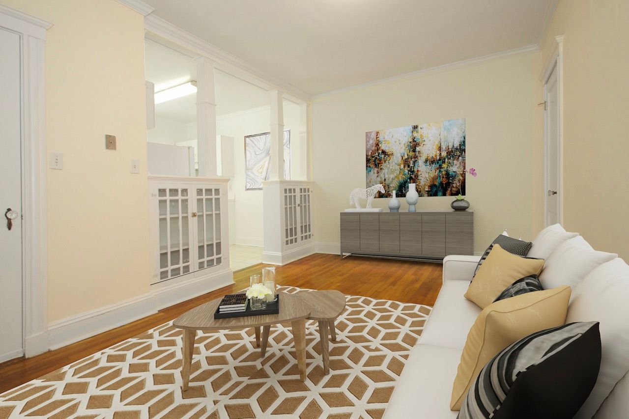 Living room in an apartment with a white sofa, beige geometric rug, wood floors, and a gray sideboard.
