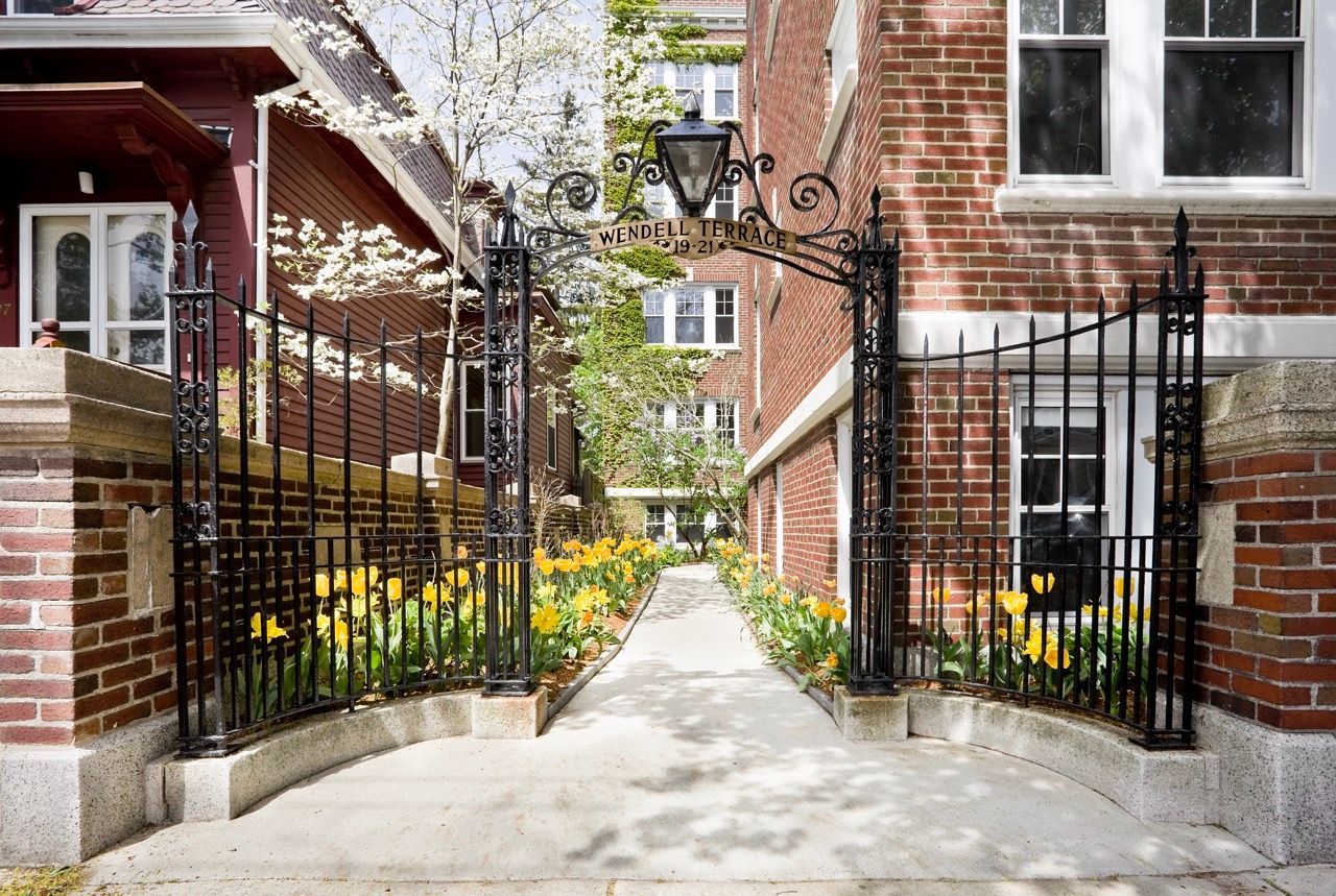 Wrought-iron arch gate at a brick apartment entrance with a path and tulips.