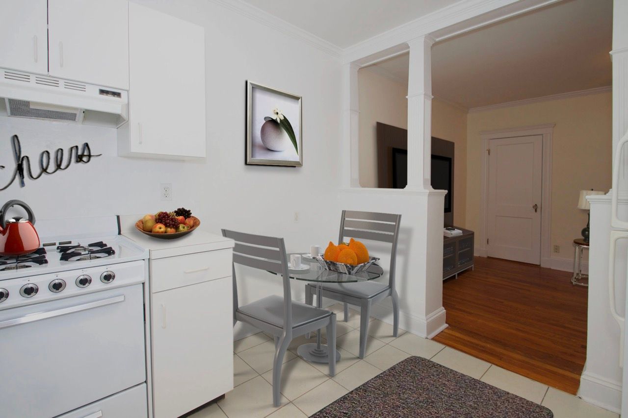 White kitchen with stove and cabinets, and a small glass dining table with two chairs.
