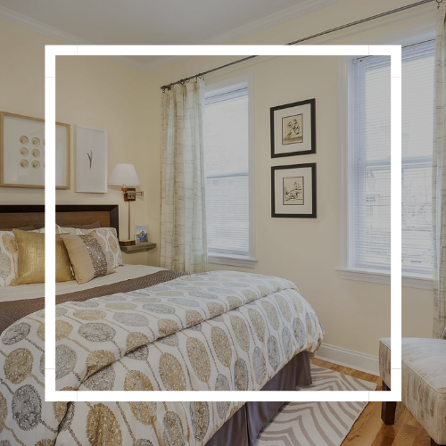 Bright bedroom with a bed, patterned bedding, two windows, and framed wall art