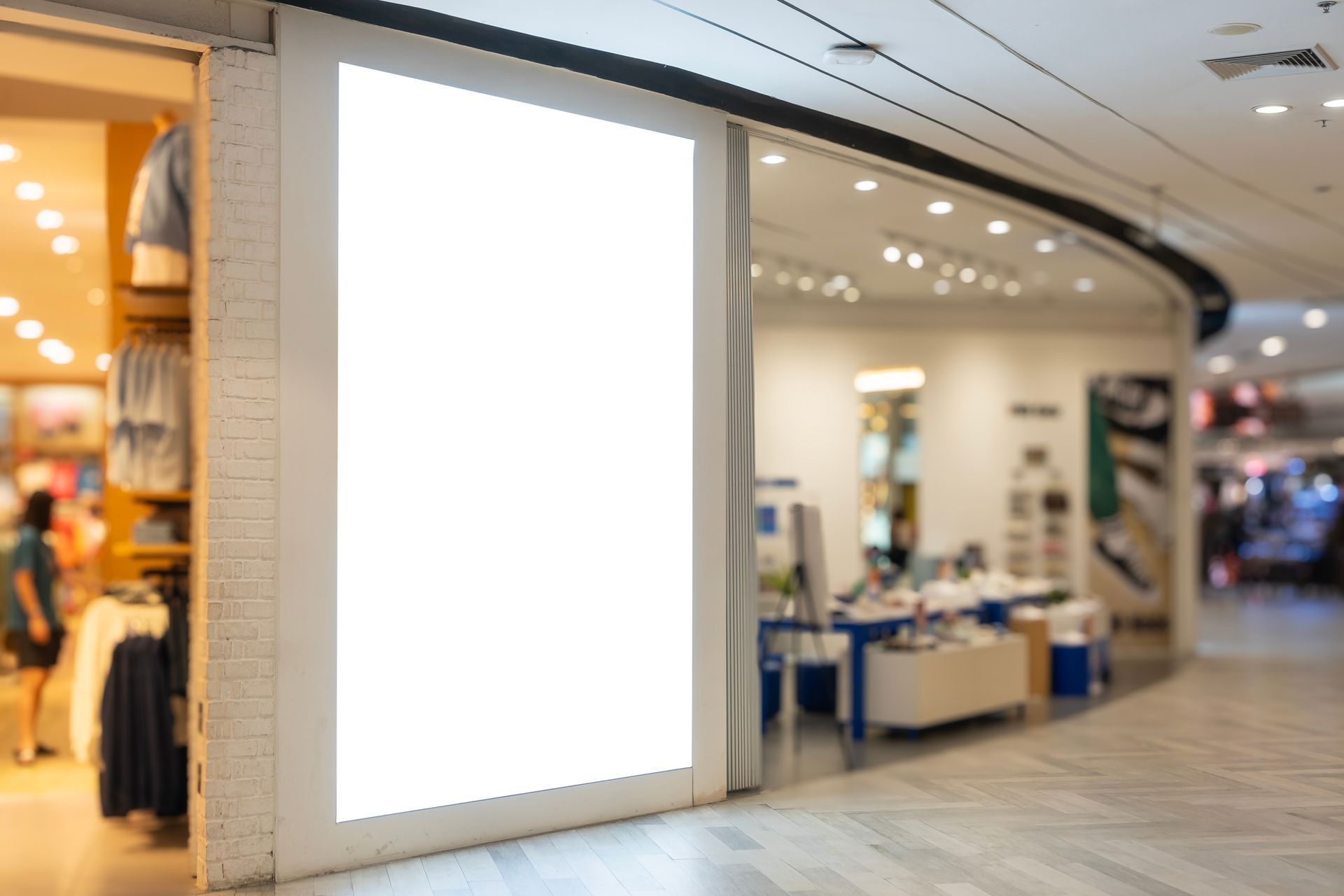 Bright blank storefront display in a shopping mall corridor with nearby clothing and retail shops