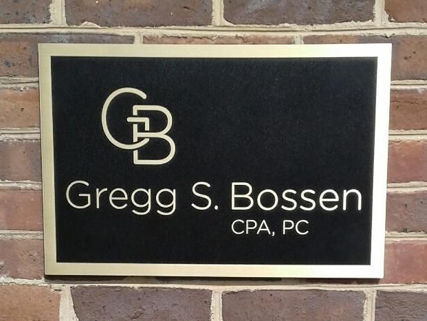 Sign for Gregg S. Bossen CPA, PC: Black plaque with gold lettering and logo on a brick wall.