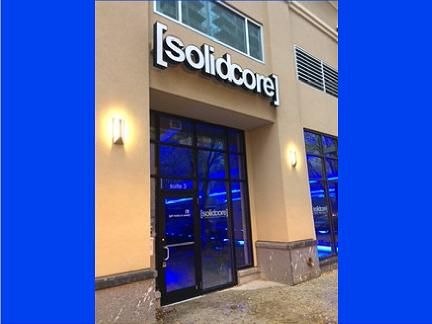 Exterior of a [solidcore] studio with blue lighting, black door, and white signage.