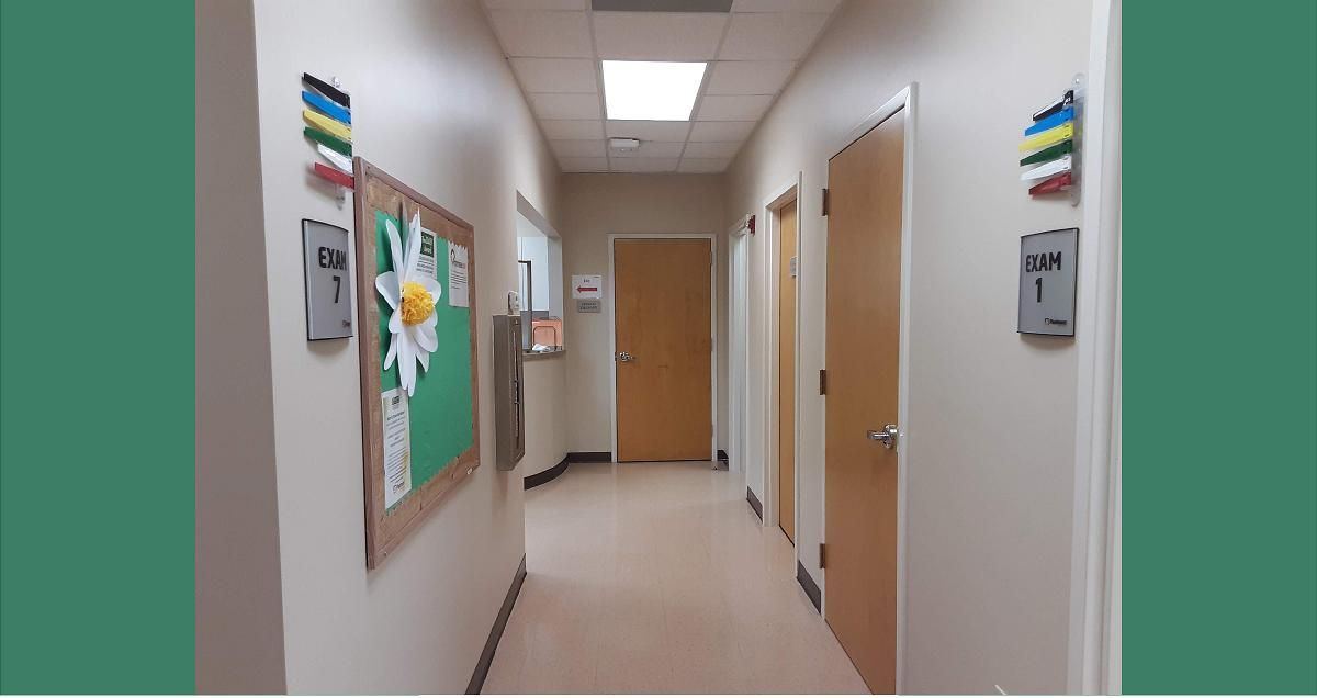 Hallway with doors, bulletin board, and ceiling lights; signs with numbers posted on doors.