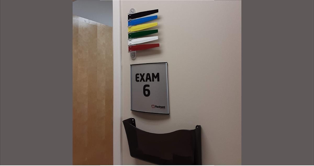 Exam room sign with a paper slot and color-coded patient status markers.