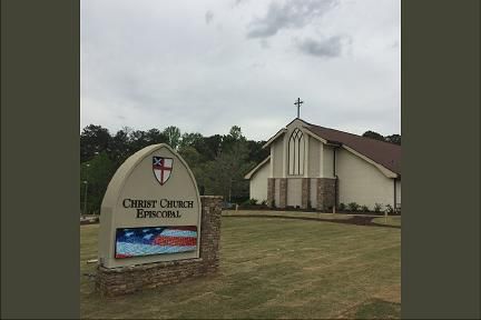 Christ Church Episcopal church building with sign on a cloudy day.