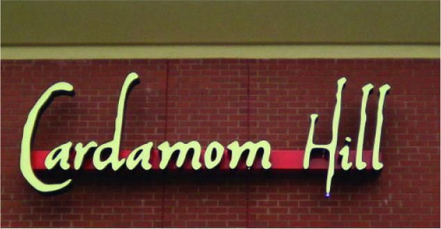 Cardamom Hill restaurant sign on brick wall, scripted white letters, red stripe.