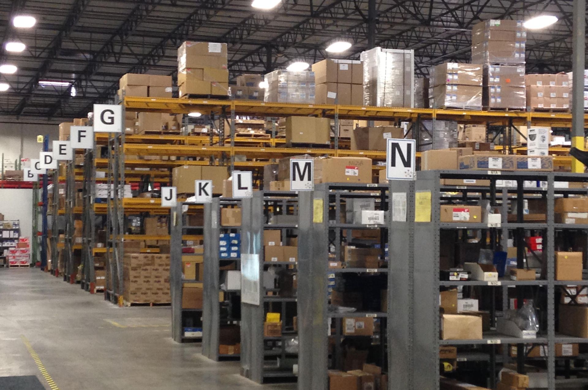 Warehouse shelves filled with boxes and parts, labeled A-N.