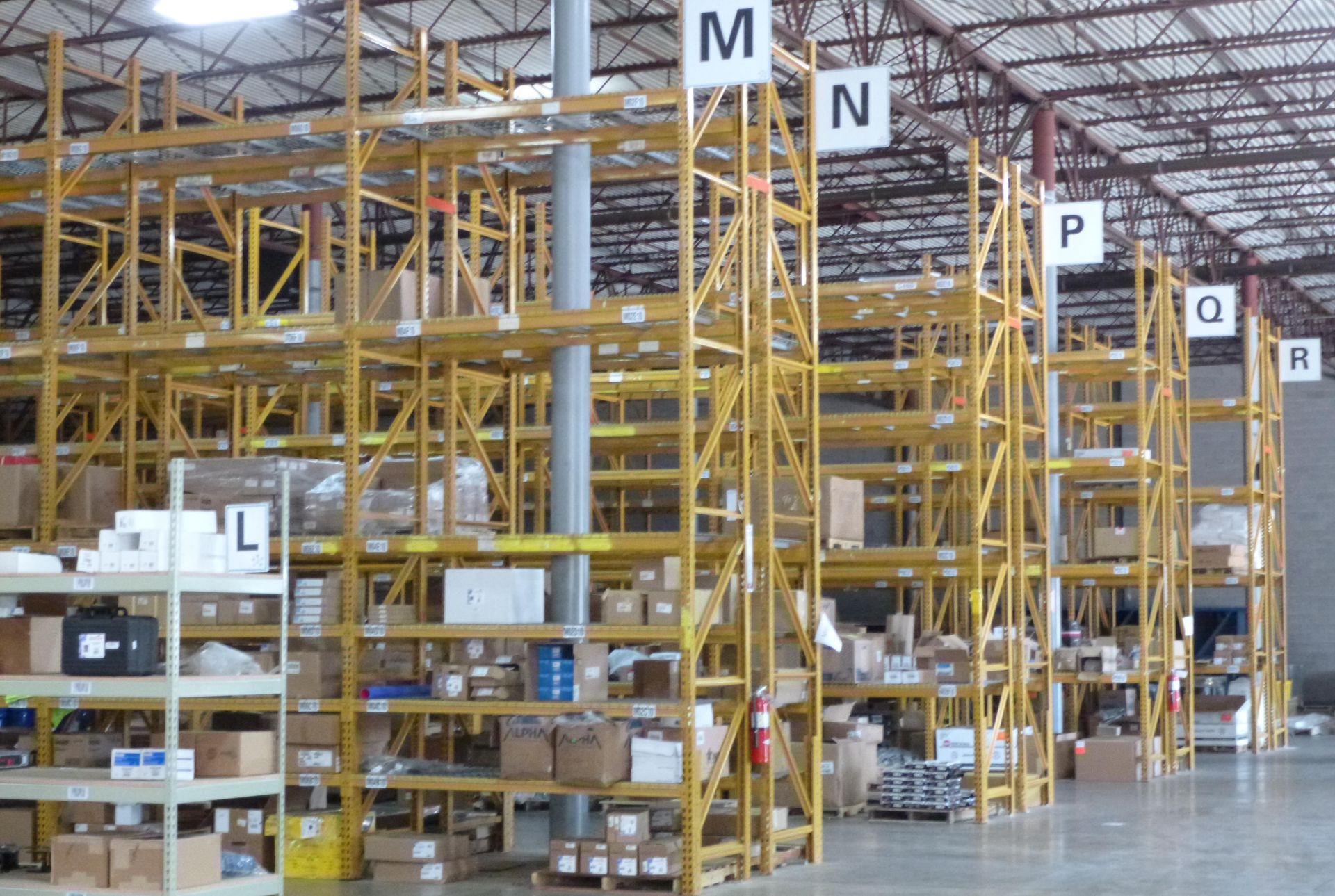 Warehouse interior with yellow shelving labeled M, N, P, Q, and R; boxes and items stored on shelves.