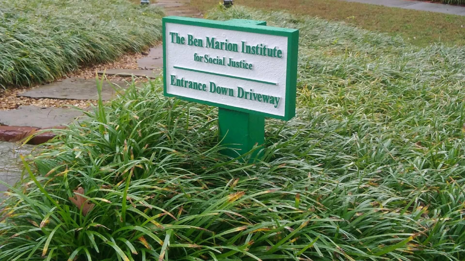 Sign for the Bon Morion Institute for Social Justice, with the entrance down the driveway. Green and white sign.