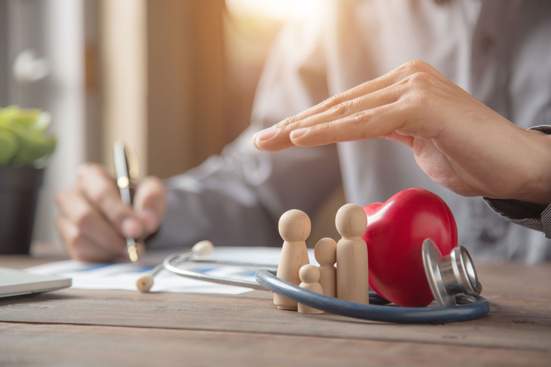 Hands over a heart-shaped object beside a clipboard and stethoscope on a desk