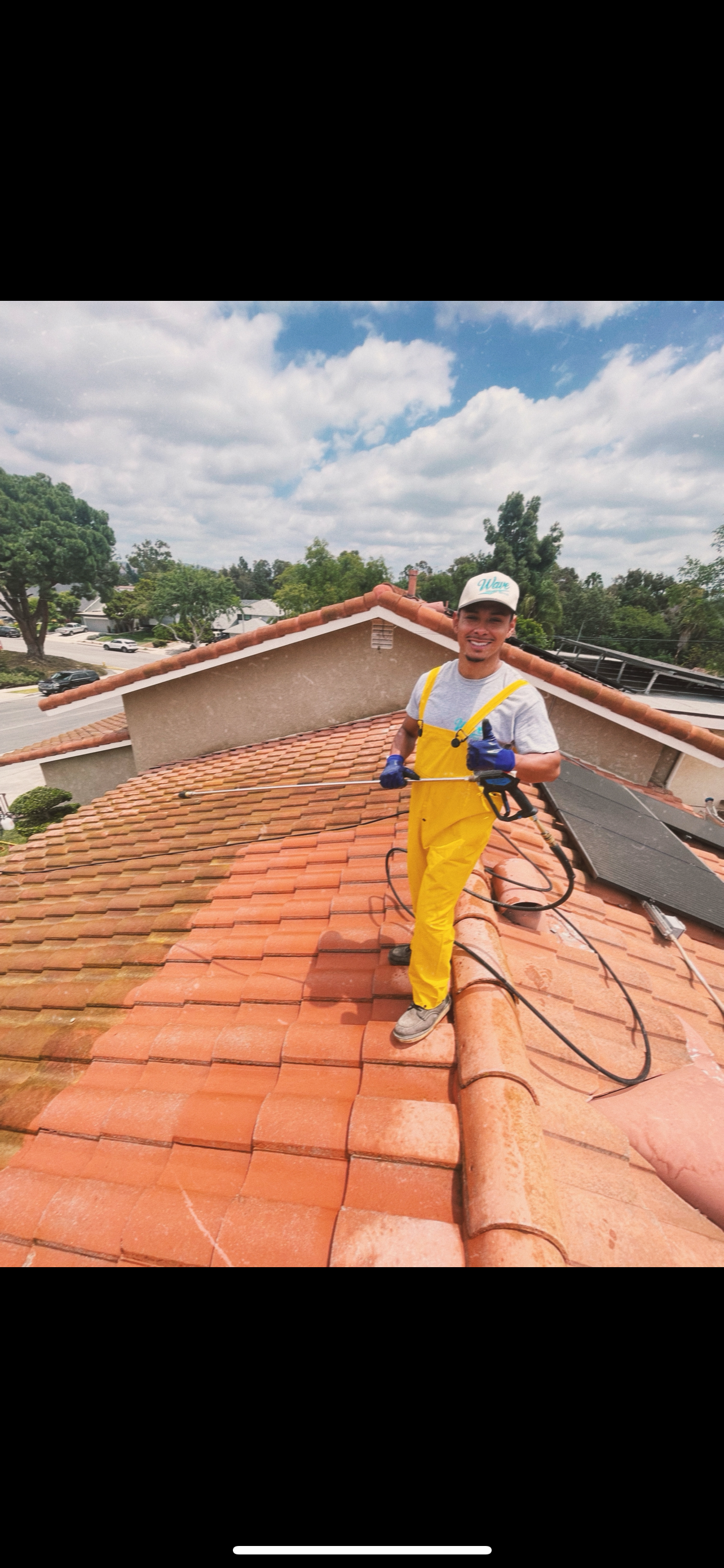 Hand holding a pressure washer spraying water along a sloped roof and gutter
