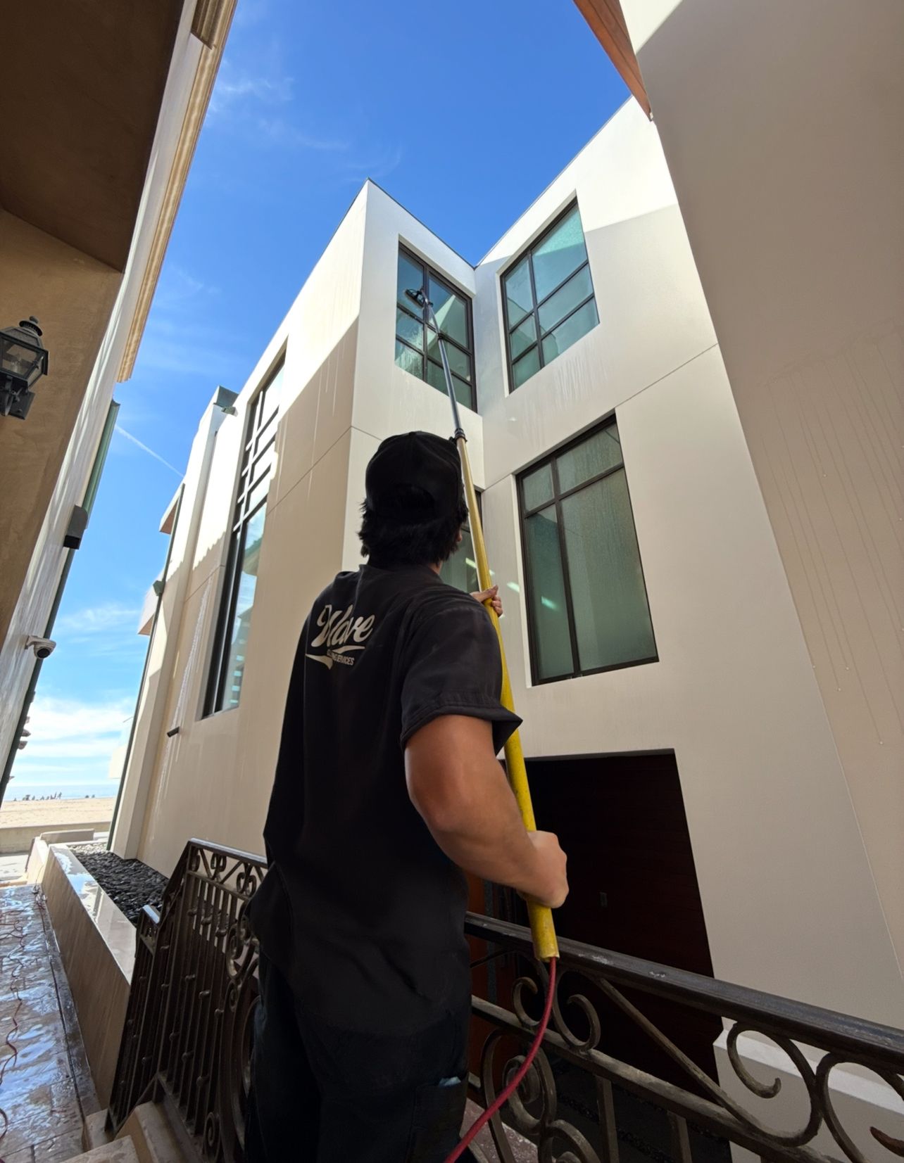 Worker pressure washing the front walkway of a large beige house with stone accents under a cloudy sky