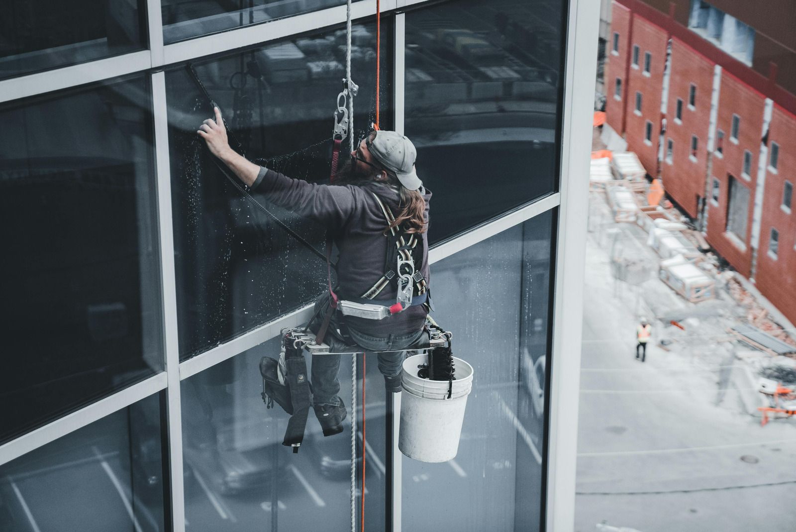 Worker suspended on a rope cleans a glass high-rise window beside a snowy street below