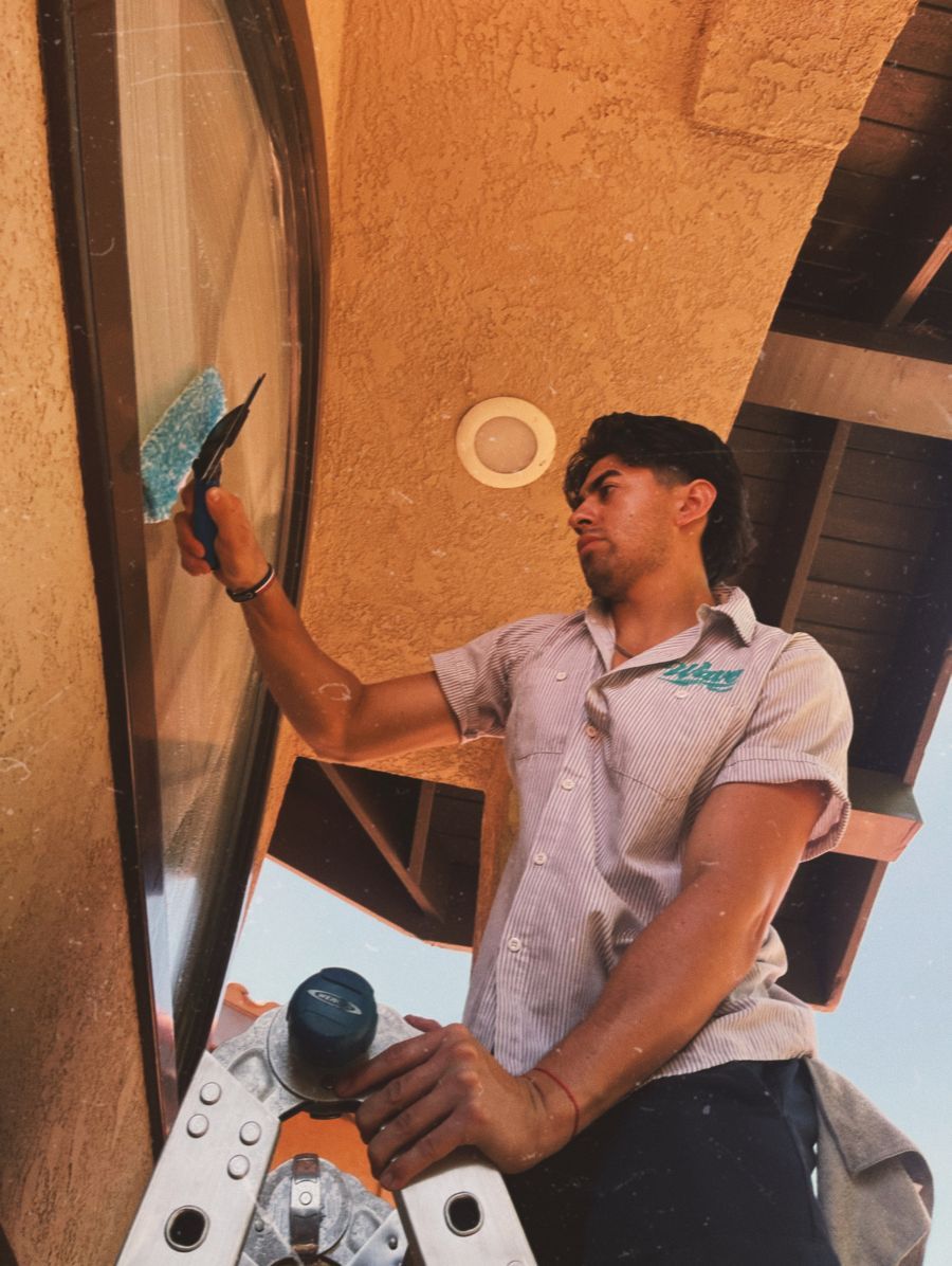 Person painting a wall with a blue roller on a ladder in a covered outdoor area