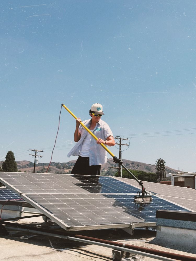 Worker cleaning solar panels on a rooftop under a clear blue sky
