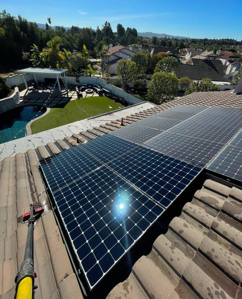 Solar panels installed on a tiled rooftop overlooking a suburban neighborhood and pool.
