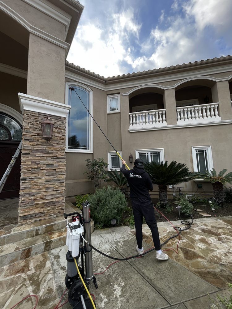 Worker pressure-washing the driveway of a two-story stucco house with stone columns and balconies