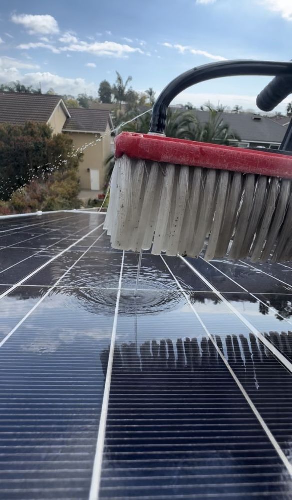Roof solar panels being cleaned with a brush under a blue sky.