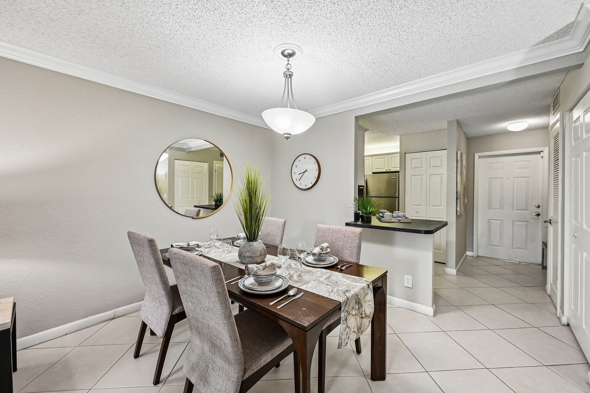 Bright dining room with a set table, chandelier, mirror, and kitchen entry in the background.