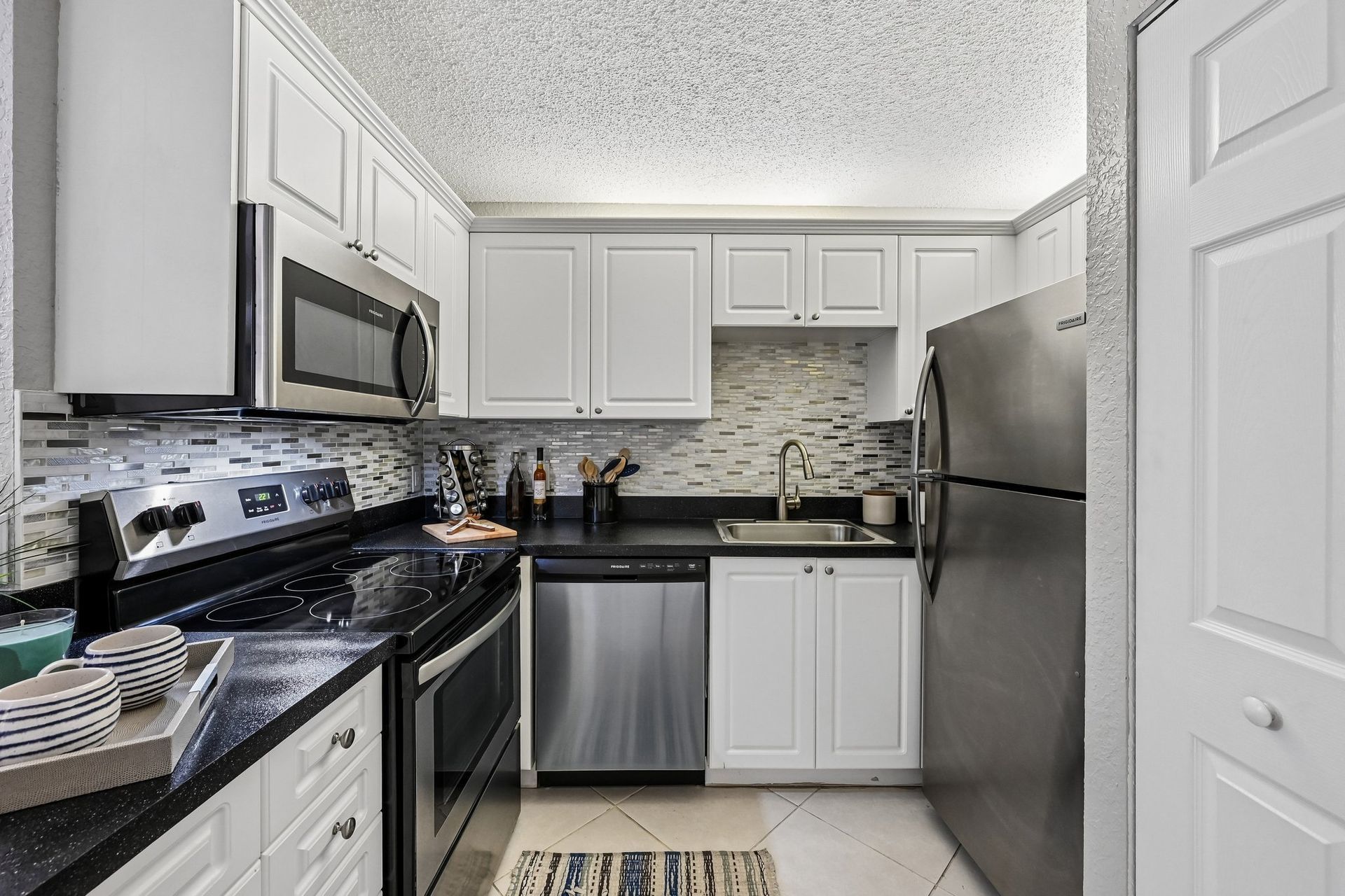 Bright modern kitchen with white cabinets, black countertops, stainless steel appliances, and tiled backsplash.