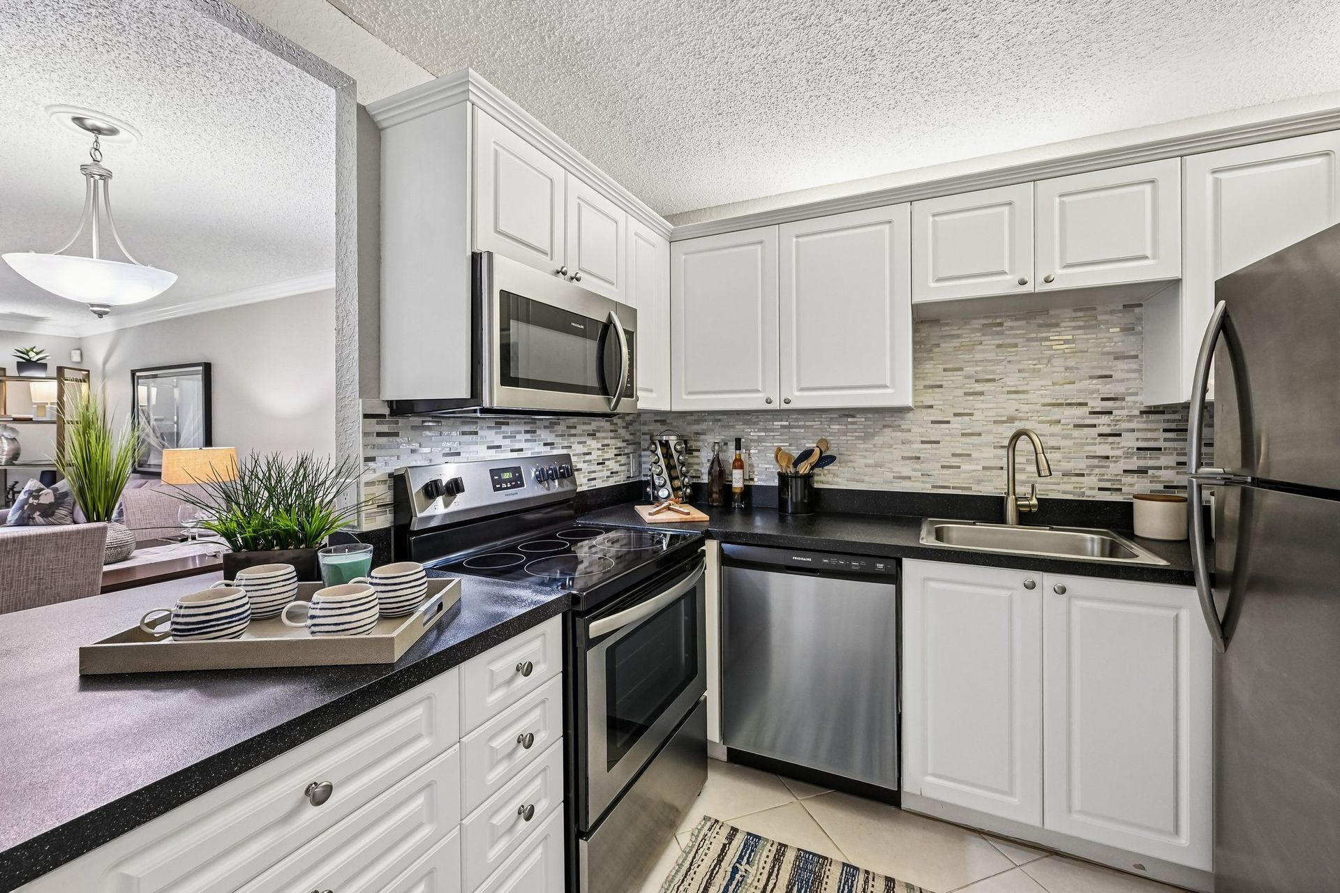 Modern white kitchen with stainless steel appliances, black countertops, and mosaic tile backsplash.