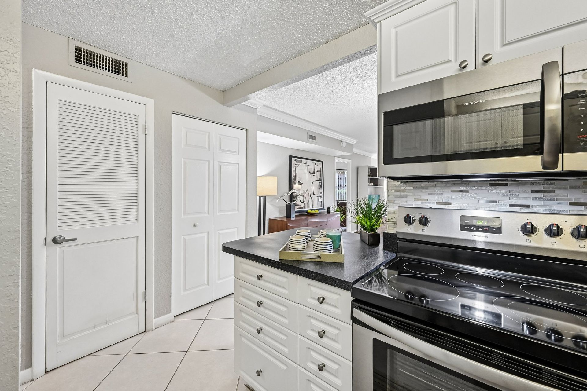 Bright kitchen with white cabinets, stainless steel stove, and a small island with a potted plant.