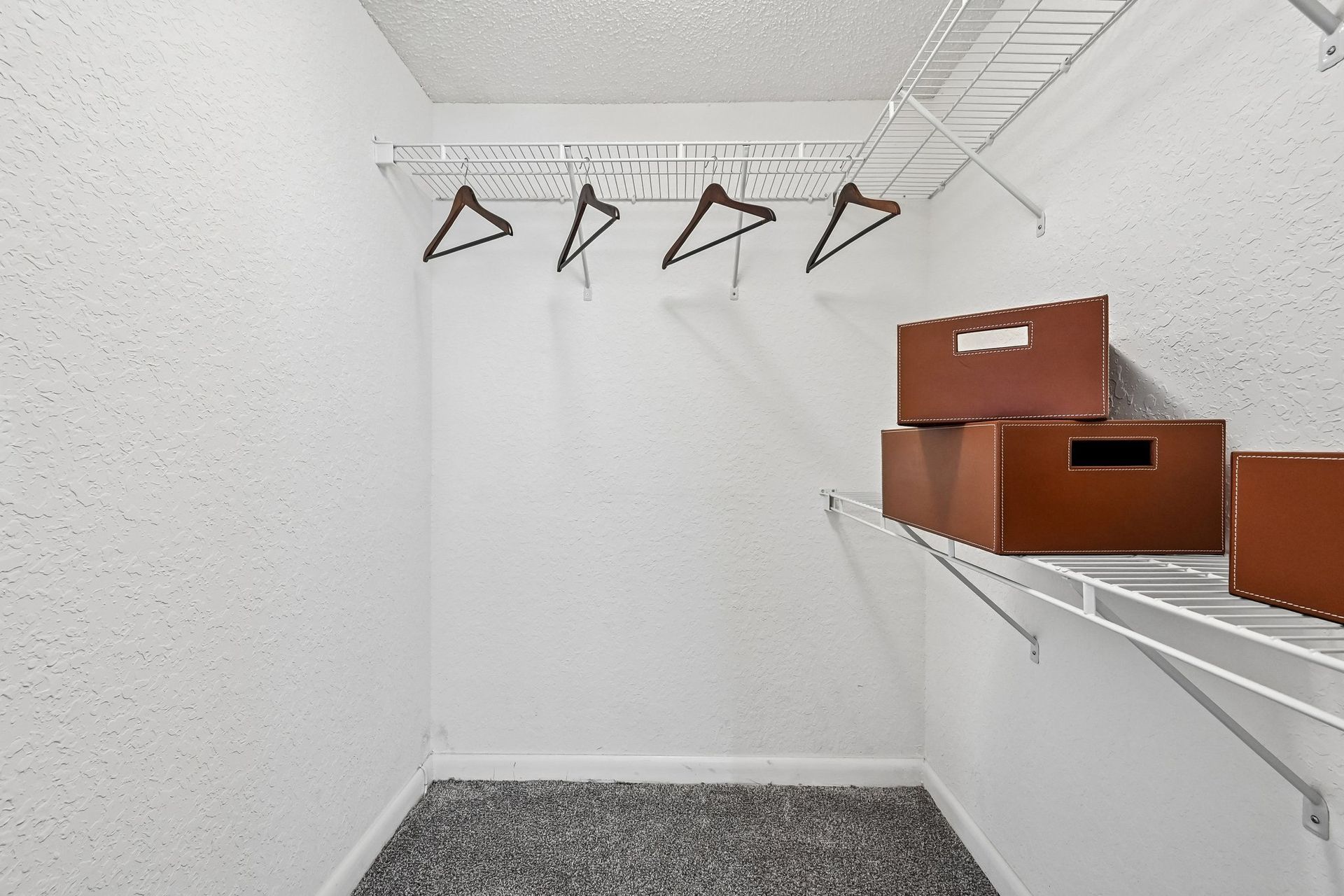 Empty white closet with wire shelves, wooden hangers, and brown storage boxes on the right.