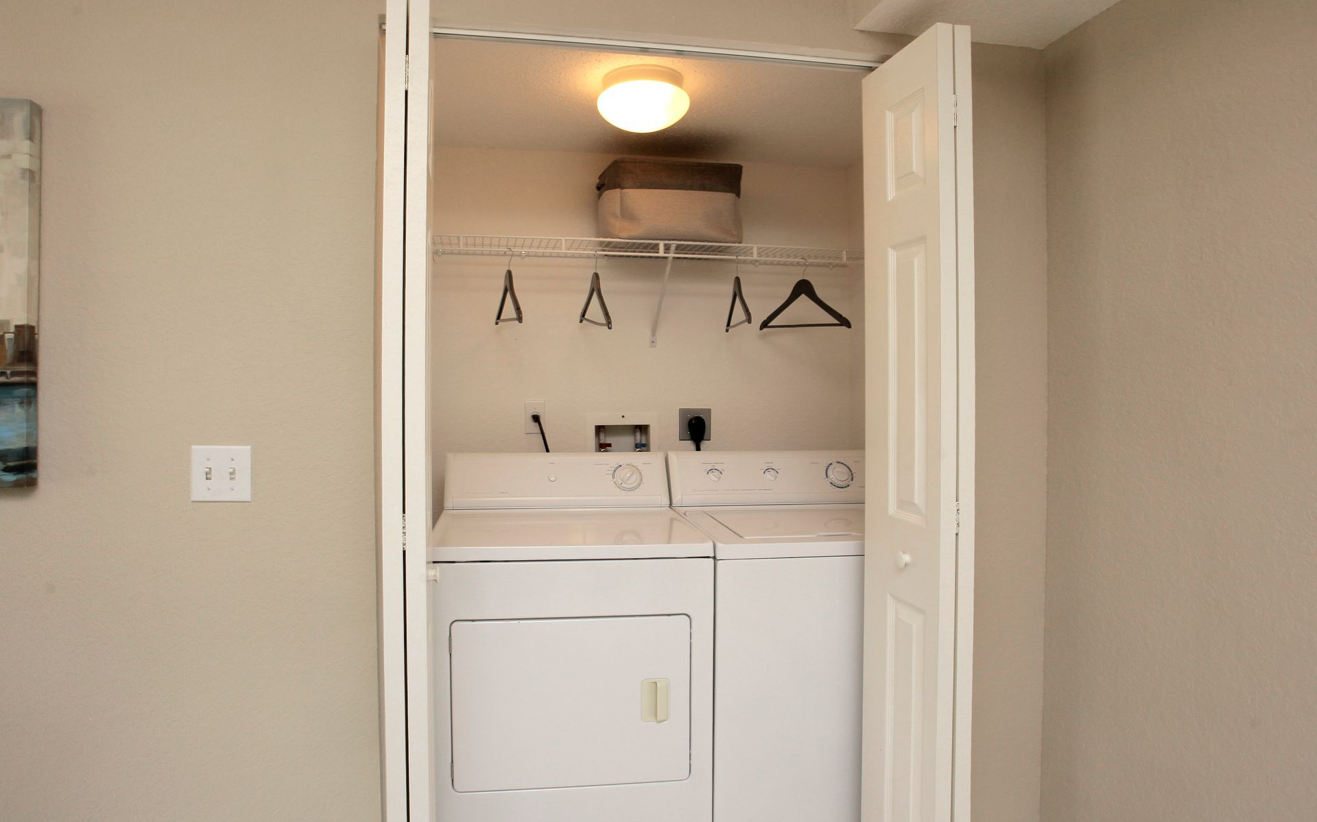 Laundry nook with stacked washer and dryer, white cabinets, and overhead light in a hallway alcove.