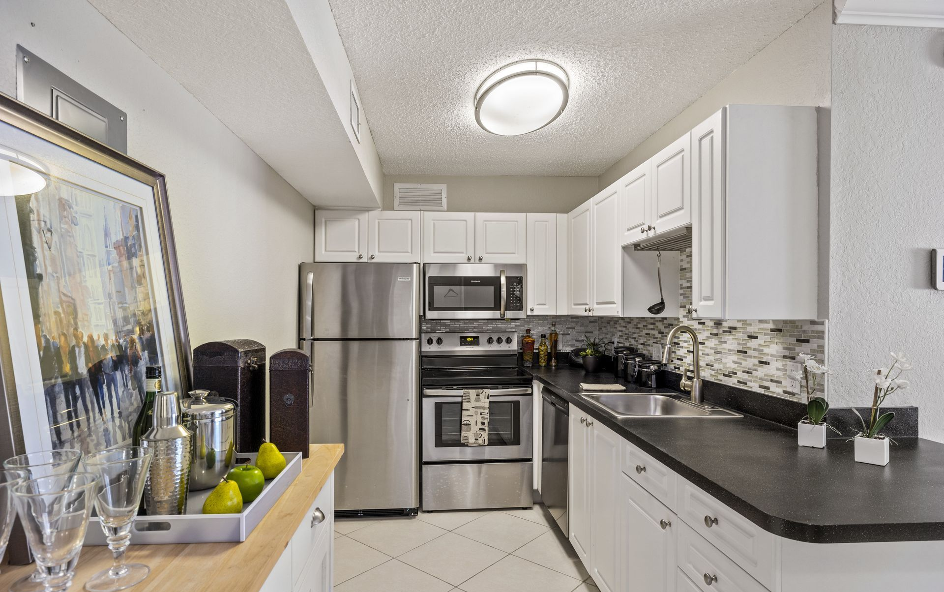 Bright modern kitchen with white cabinets, stainless appliances, black countertops, and a dining table in front.