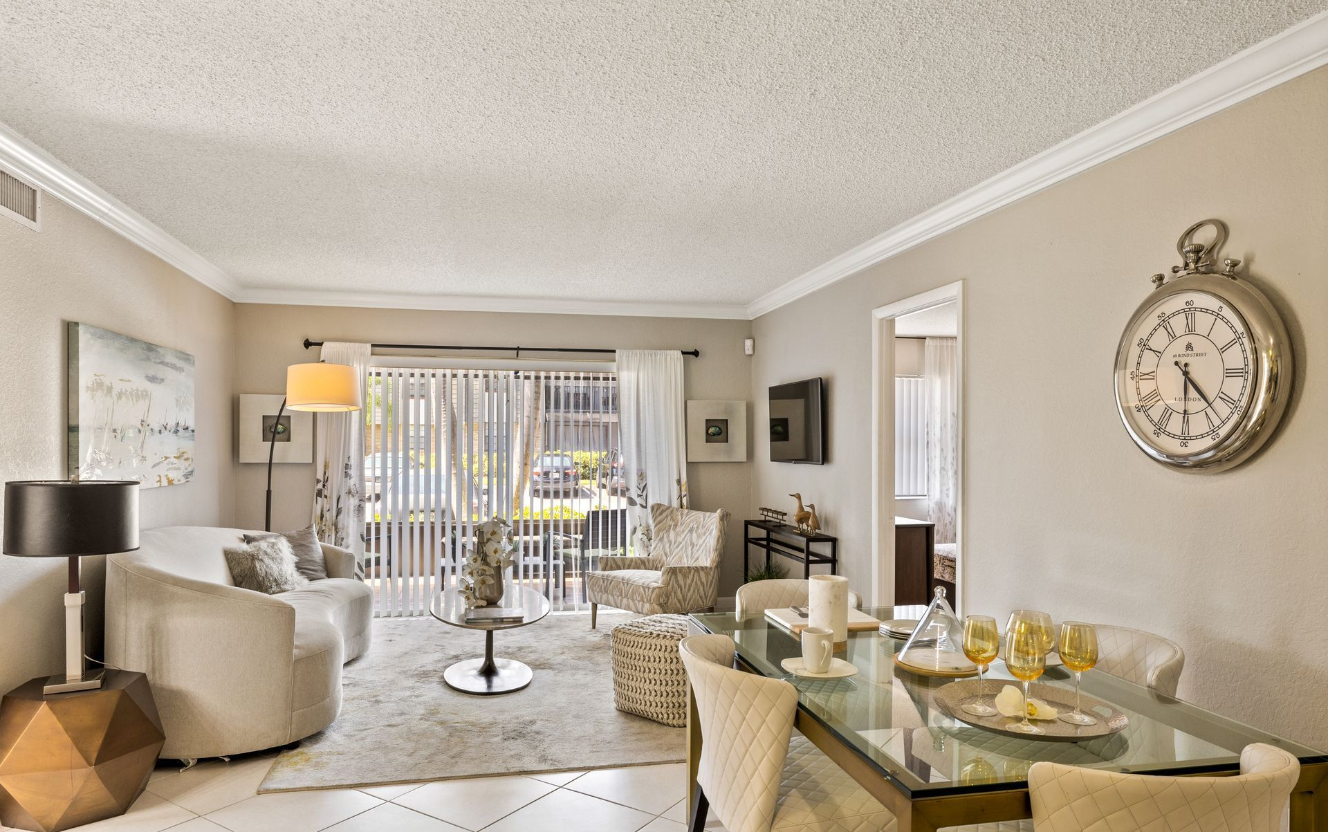 Bright living room with beige chairs, glass dining table, and sliding doors to a patio.