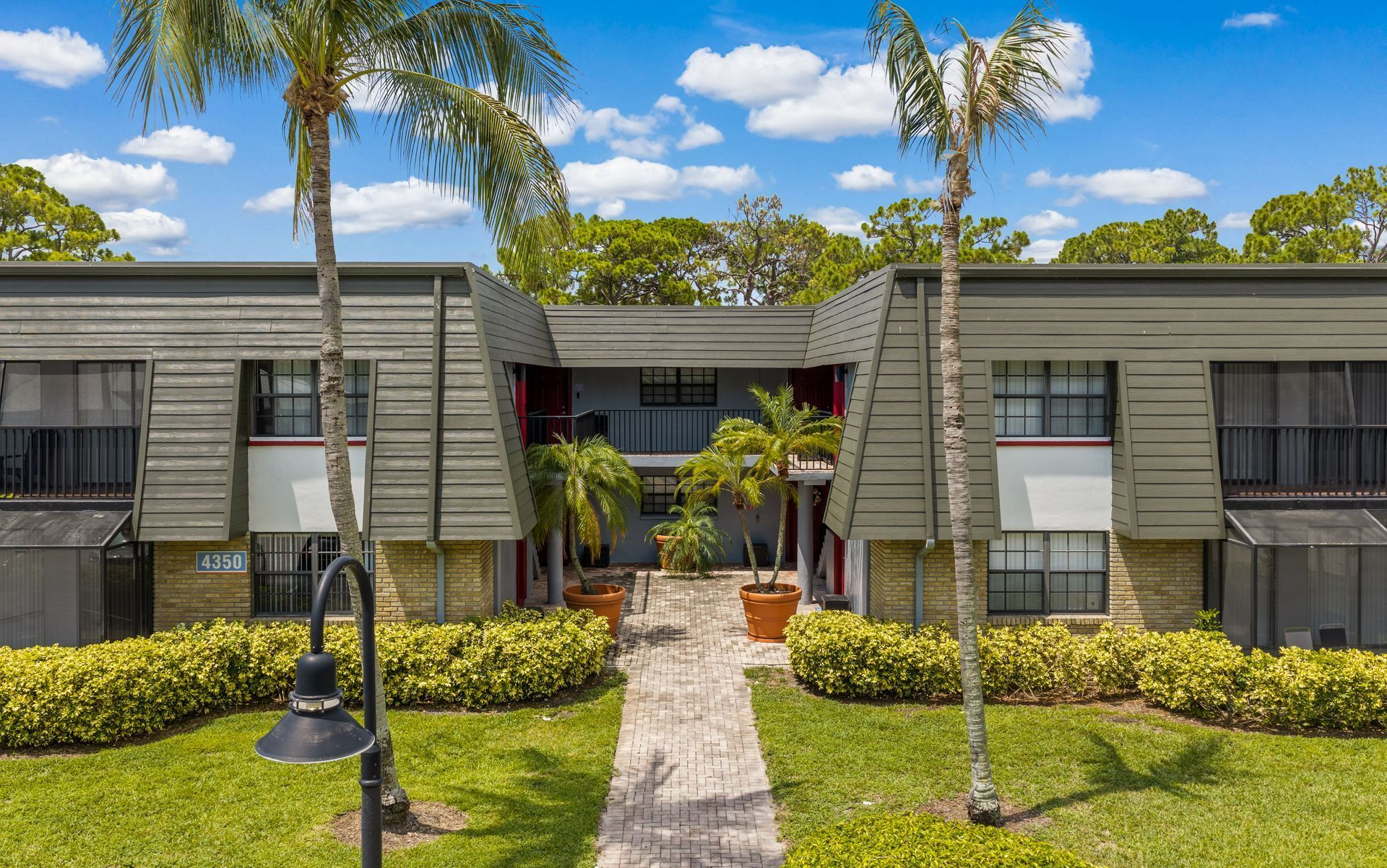 Apartment building with palm trees, central walkway, and landscaped shrubs under a blue sky.