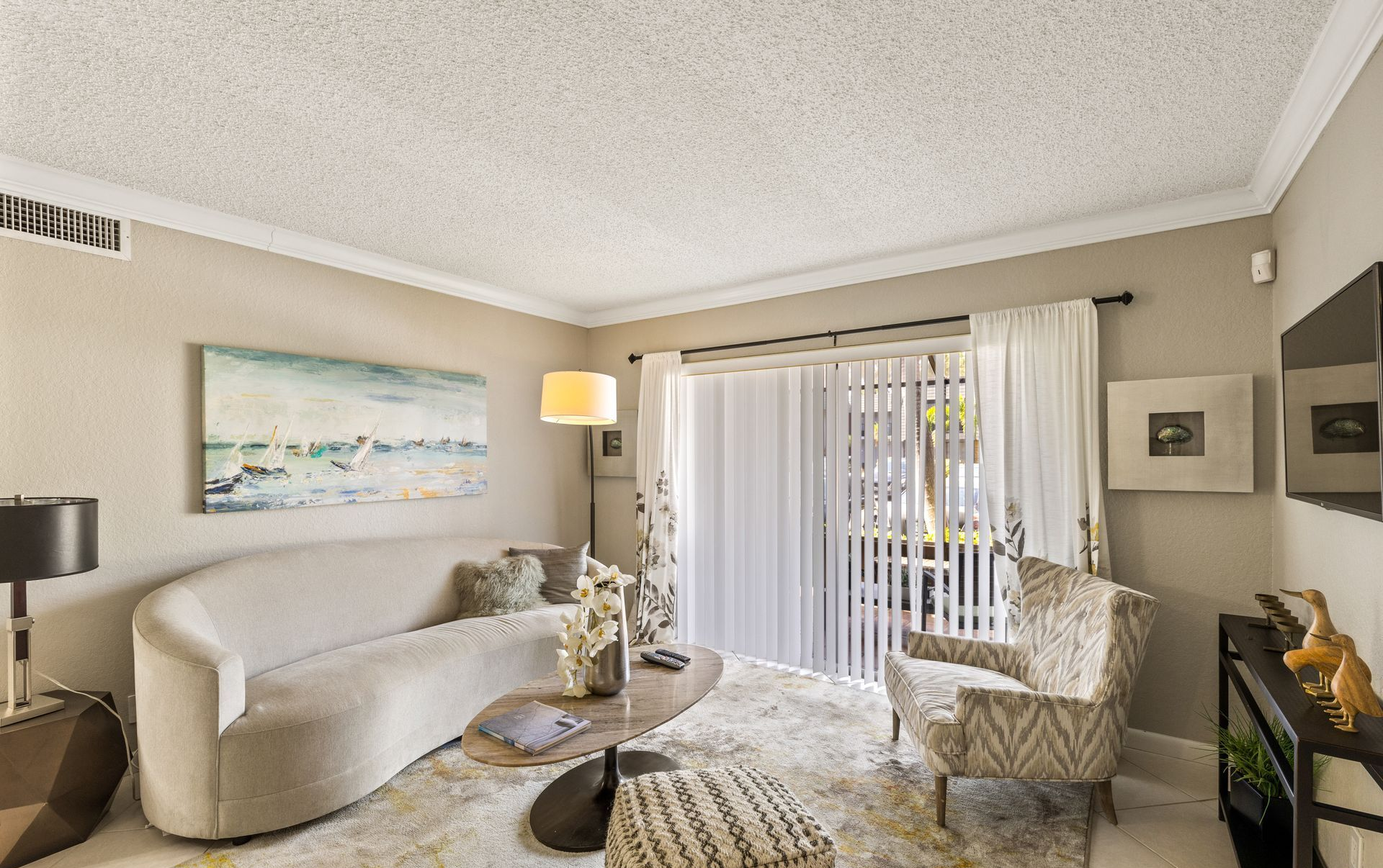 Bright living room with curved sofa, armchairs, coffee table, sliding glass doors, and neutral decor.