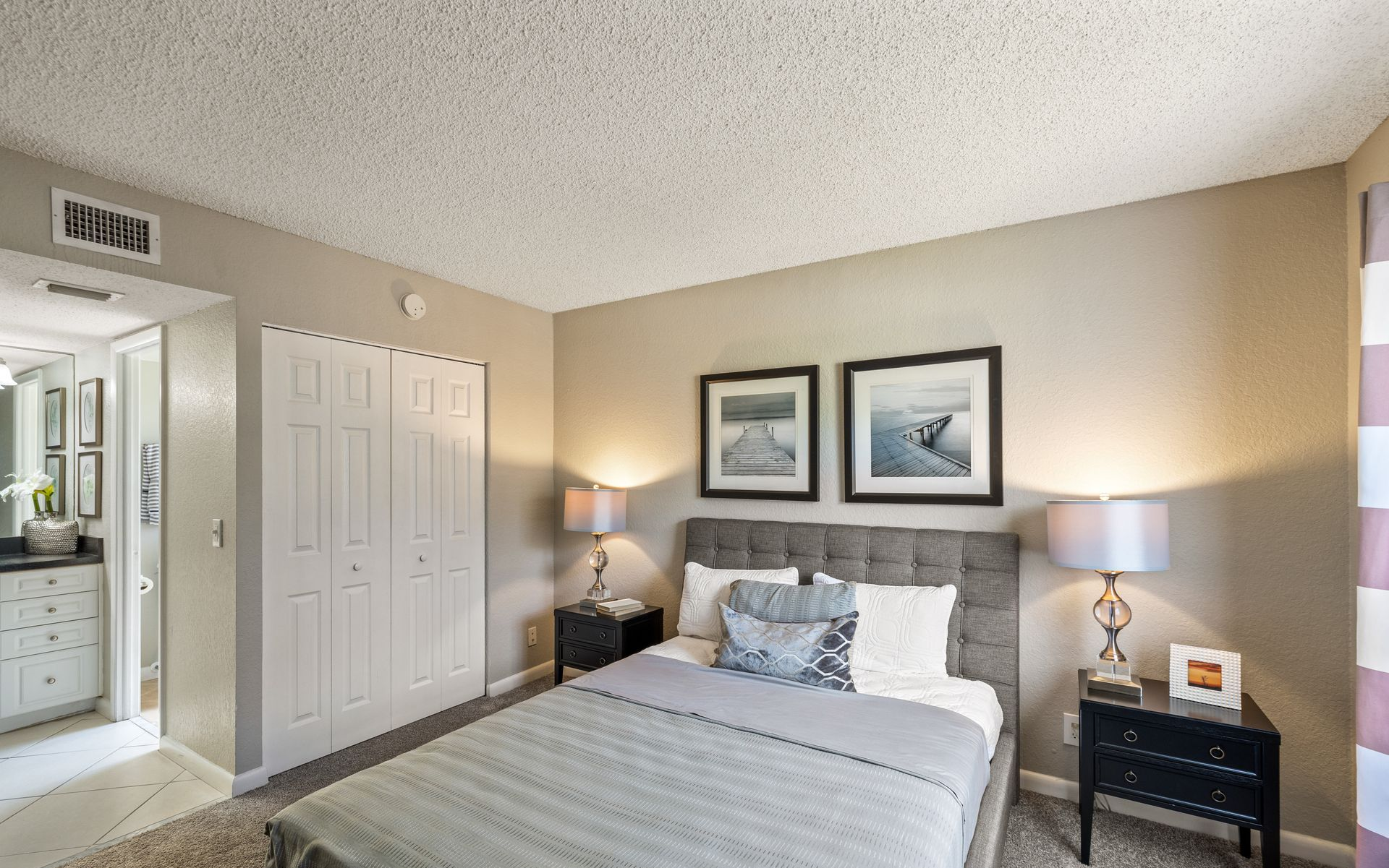 Cozy bedroom with queen bed, gray upholstered headboard, bedside lamps, and framed wall art.