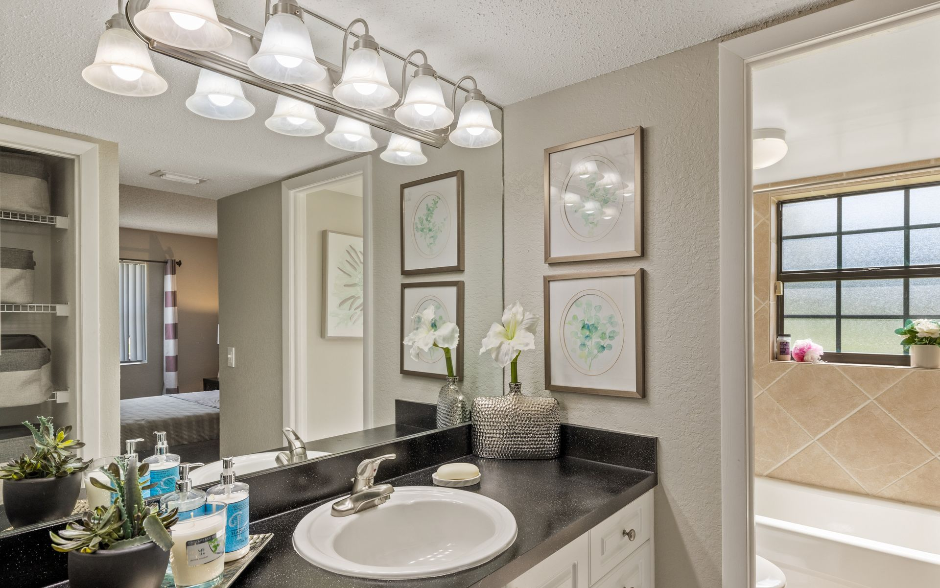 Modern bathroom vanity with granite counter, round sink, framed art, and large mirror under bright lights.