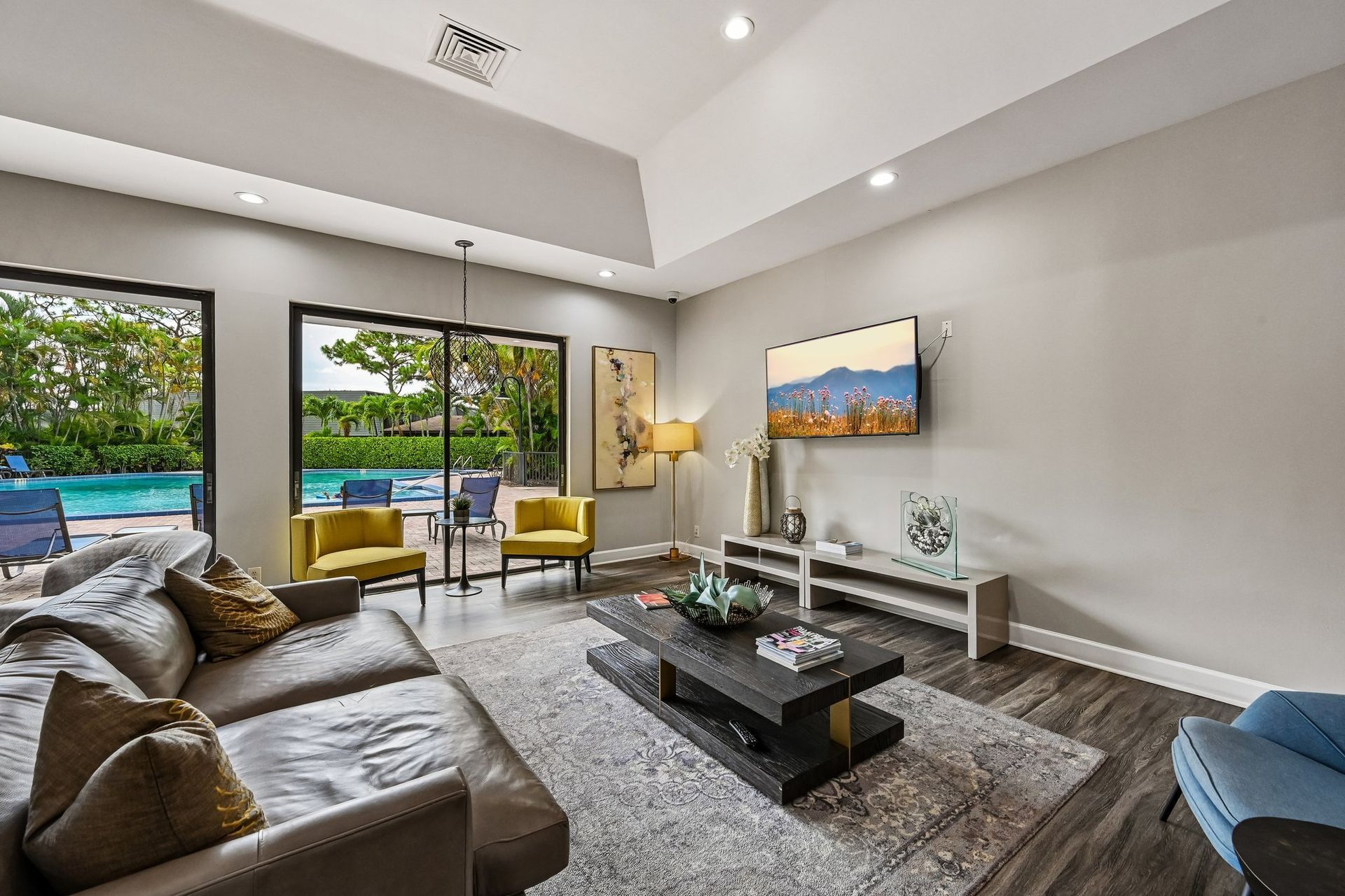 Modern living room with gray sectional, coffee table, TV console, and large windows overlooking greenery.